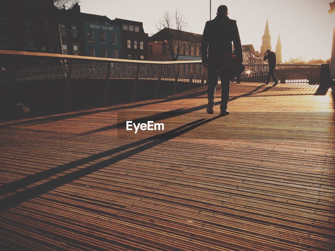 Low angle view of man walking on boardwalk during sunny day in city