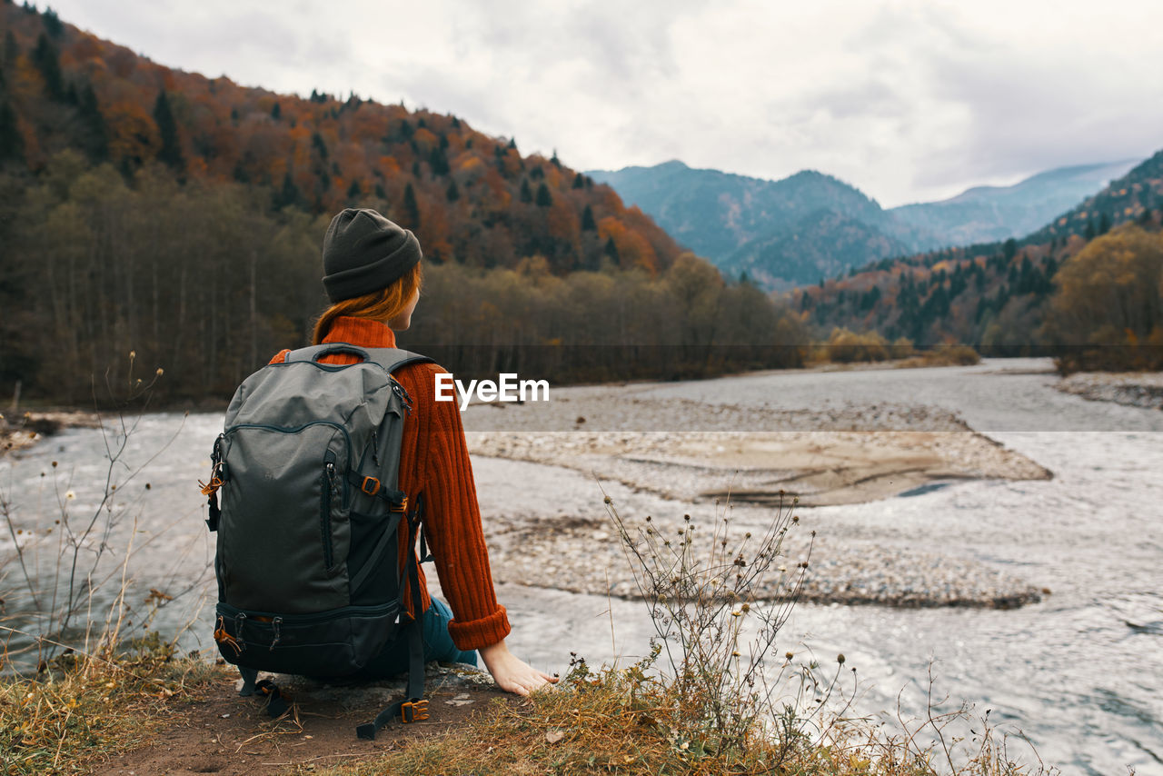 REAR VIEW OF MAN SITTING ON LANDSCAPE AGAINST MOUNTAIN