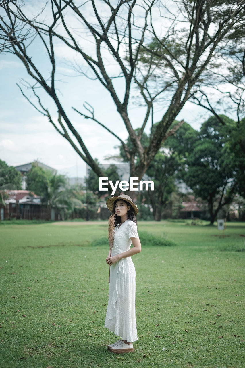 WOMAN STANDING ON FIELD AGAINST TREES