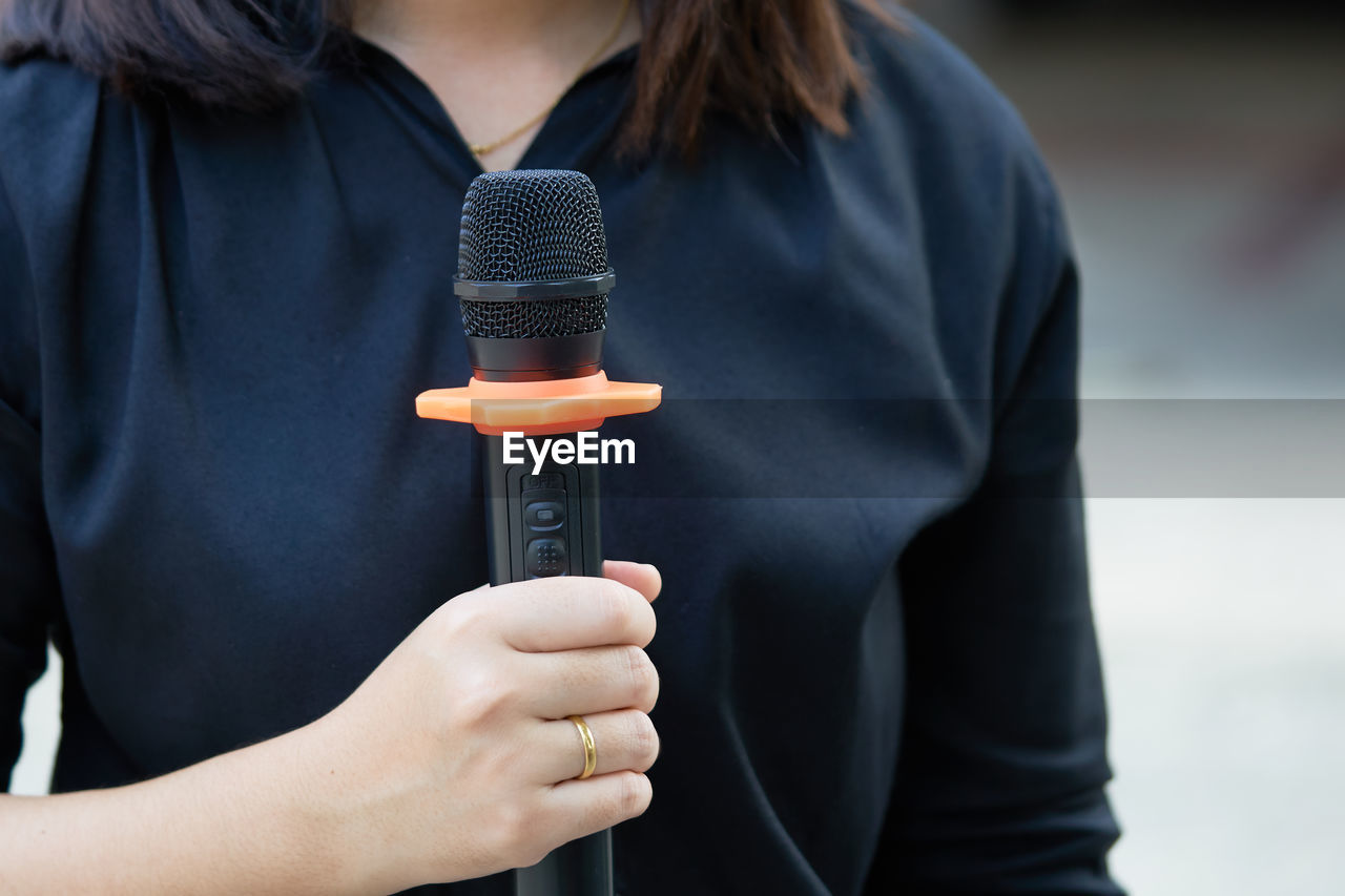 Midsection of female journalist holding microphone