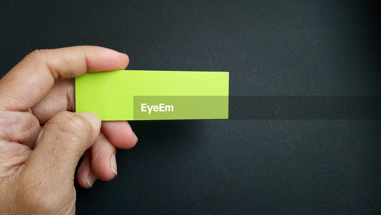 Cropped hand of person holding blank green adhesive note on table