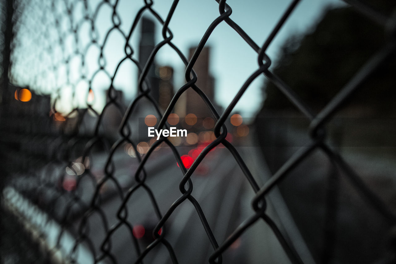 Close-up of chainlink fence against cityscape