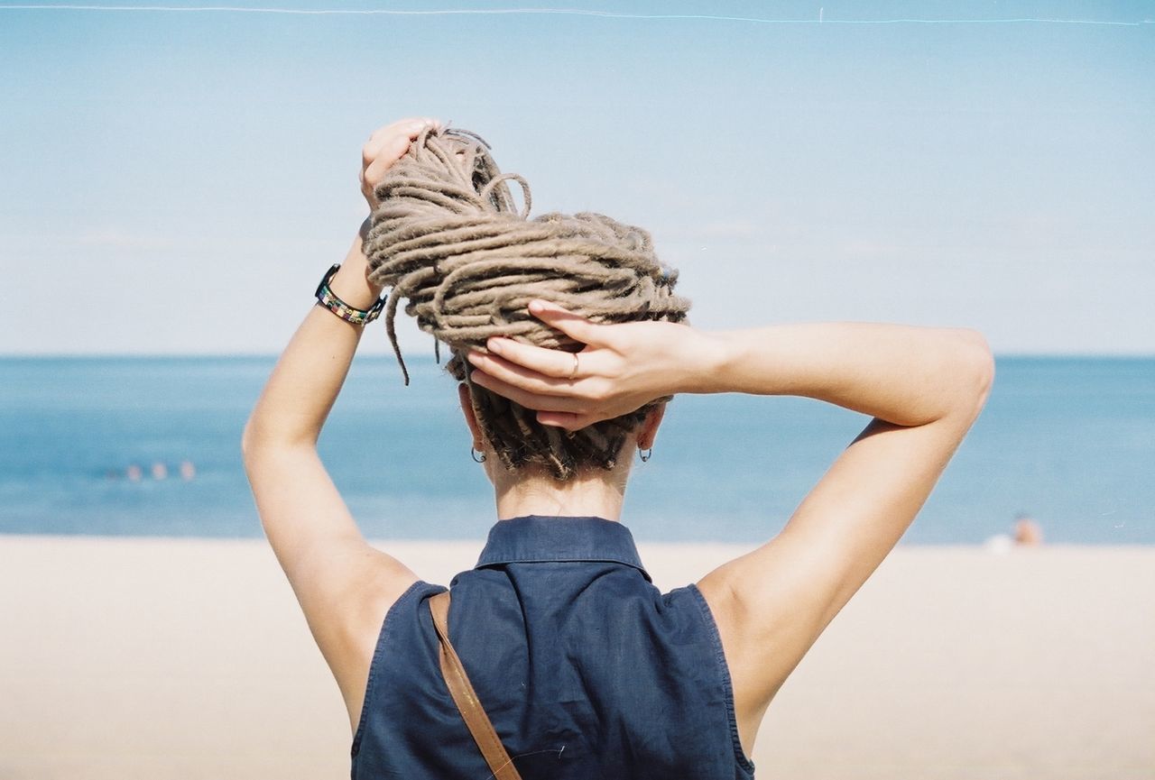 Rear view of woman holding dreadlocks at beach