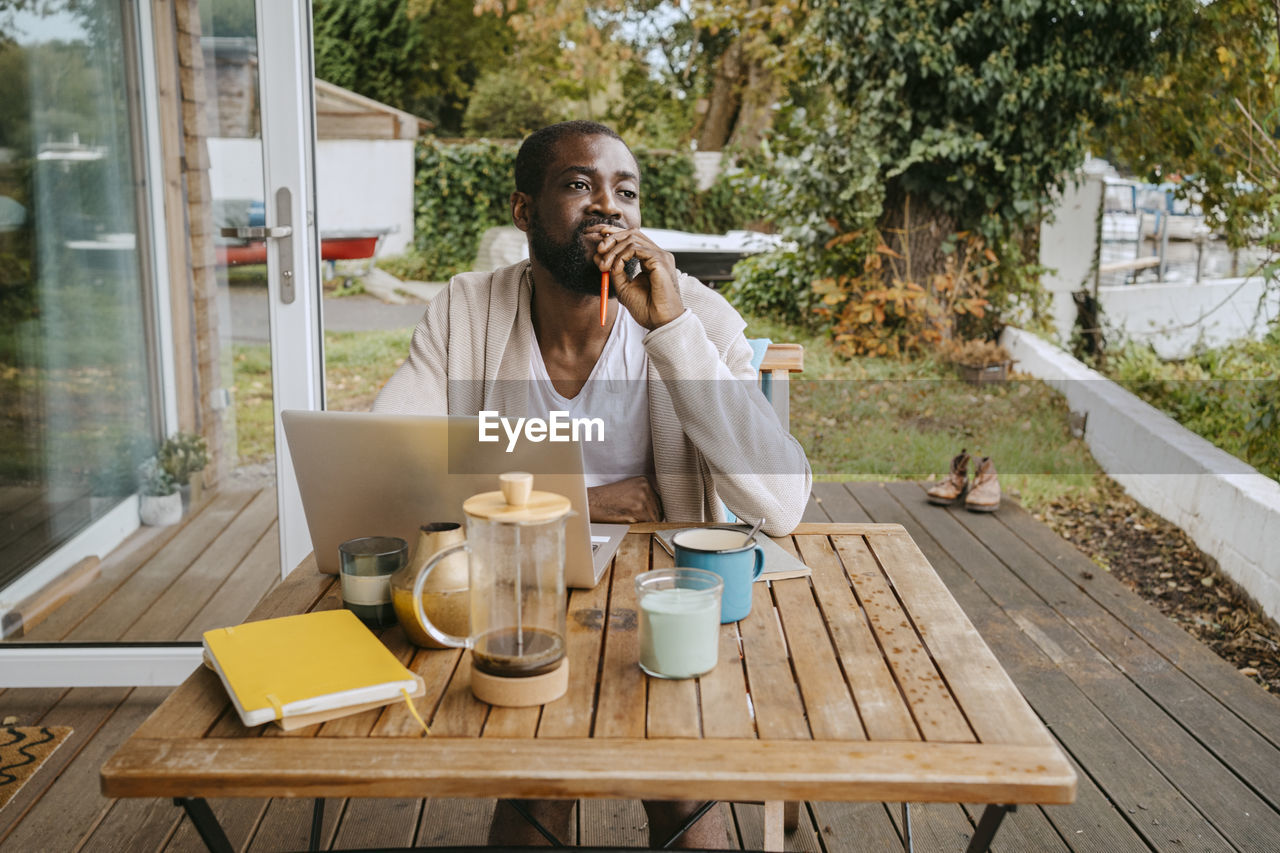 Thoughtful man with laptop sitting at table on porch