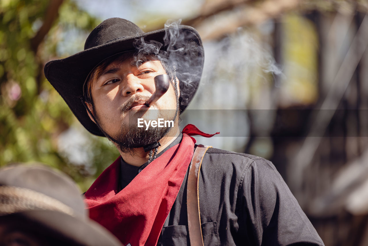 A tobacco pipe is smoked by a cowboy wearing a wide-brimmed hat and a headband.