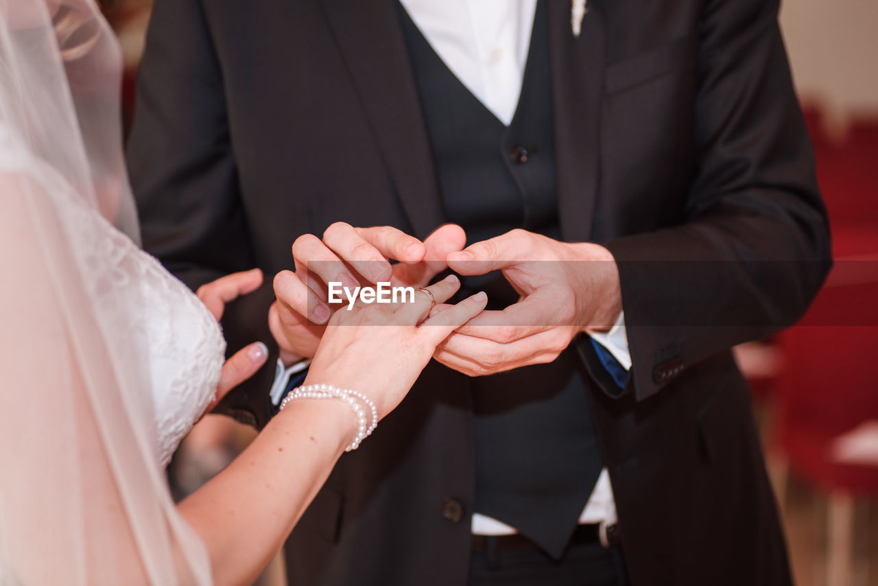 MIDSECTION OF COUPLE HOLDING HANDS IN FRONT OF MOTHER