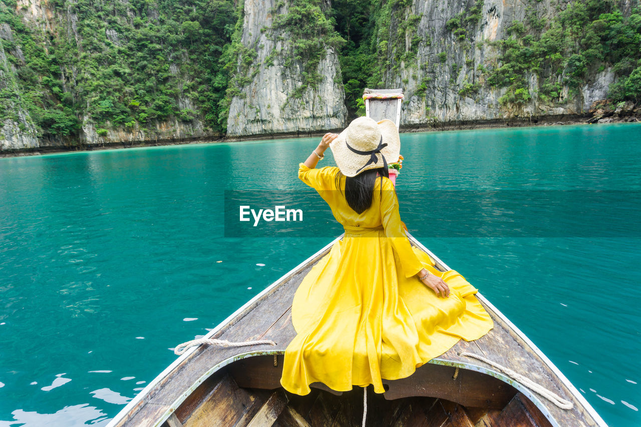 REAR VIEW OF PERSON WITH UMBRELLA ON BOAT AGAINST PLANTS