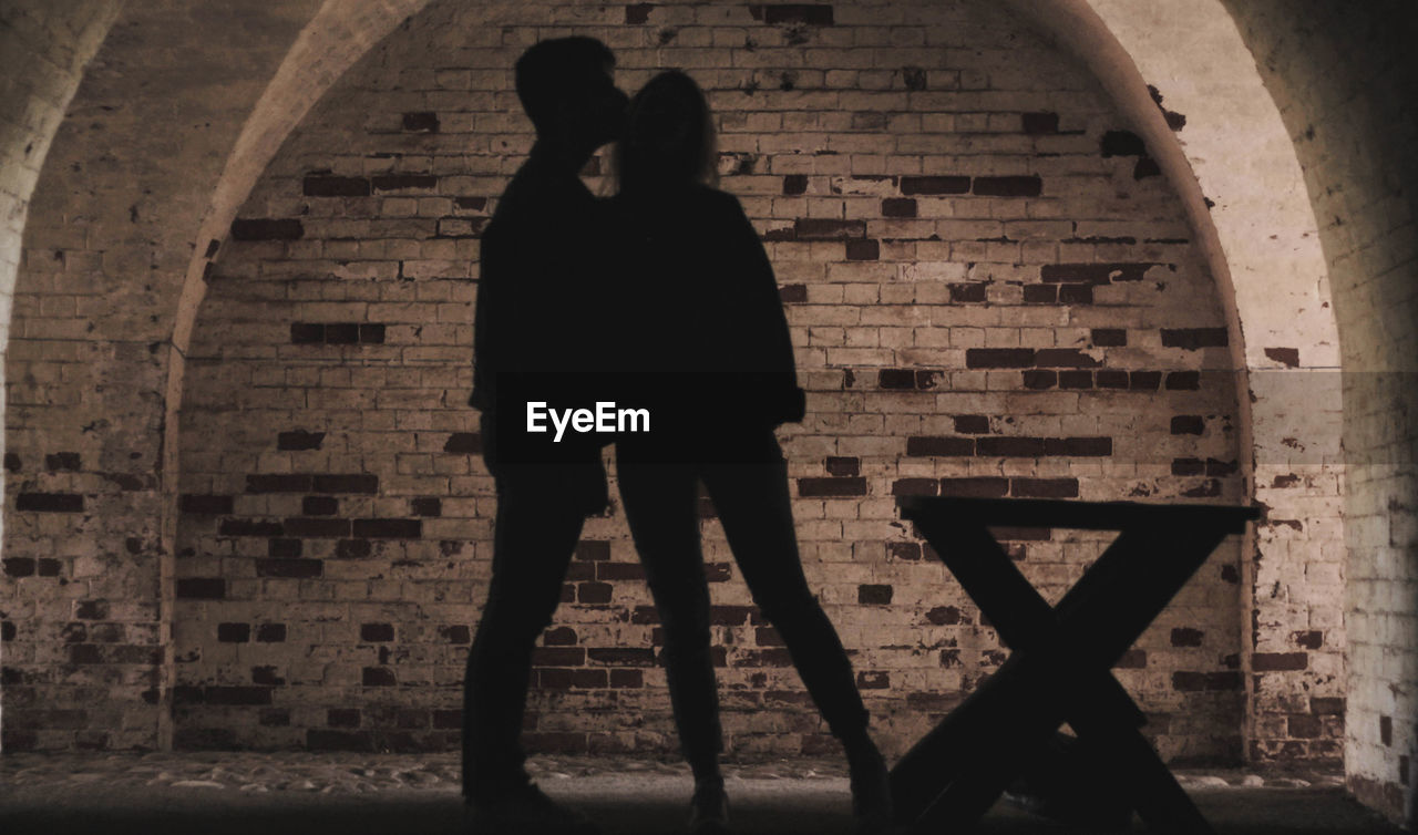 Rear view of silhouette couple standing against brick wall