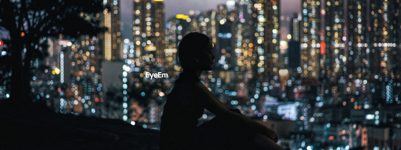 WOMAN LOOKING AT ILLUMINATED CITY AT NIGHT