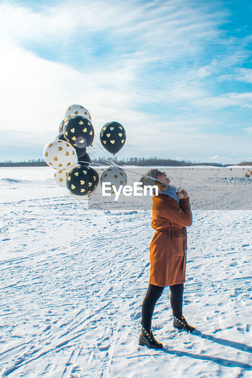 Woman with balloons standing on snow against sky