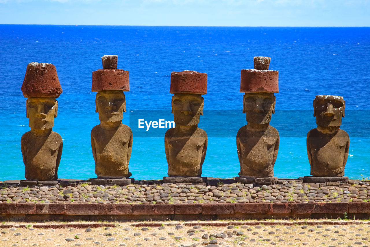 STATUES ON BEACH BY SEA AGAINST BLUE SKY