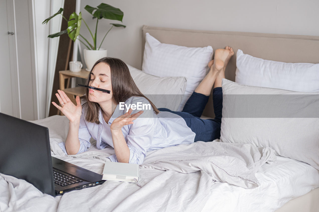 portrait of young woman using digital tablet while sitting on bed at home