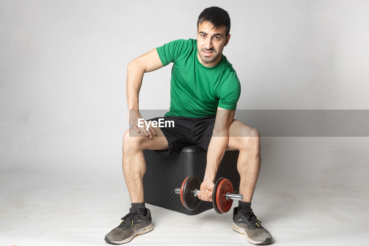 PORTRAIT OF YOUNG MAN SITTING AGAINST WALL