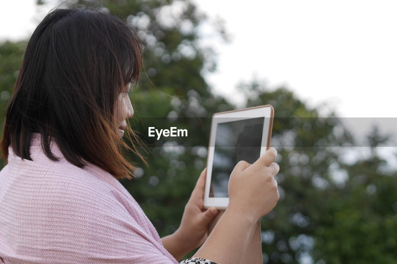 Woman using digital tablet against tree