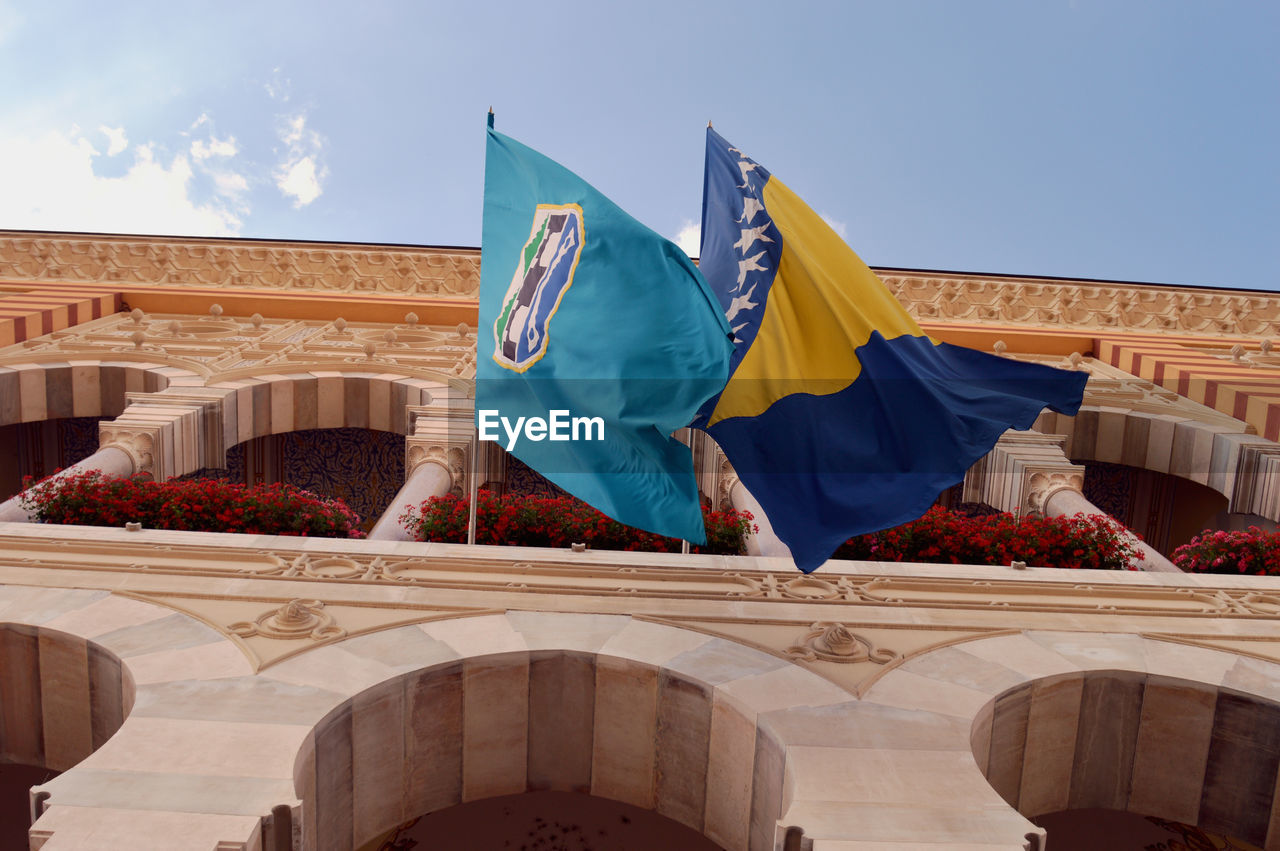 Low angle view of bosnia herzegovinan flag and coat of arms flag on historic building