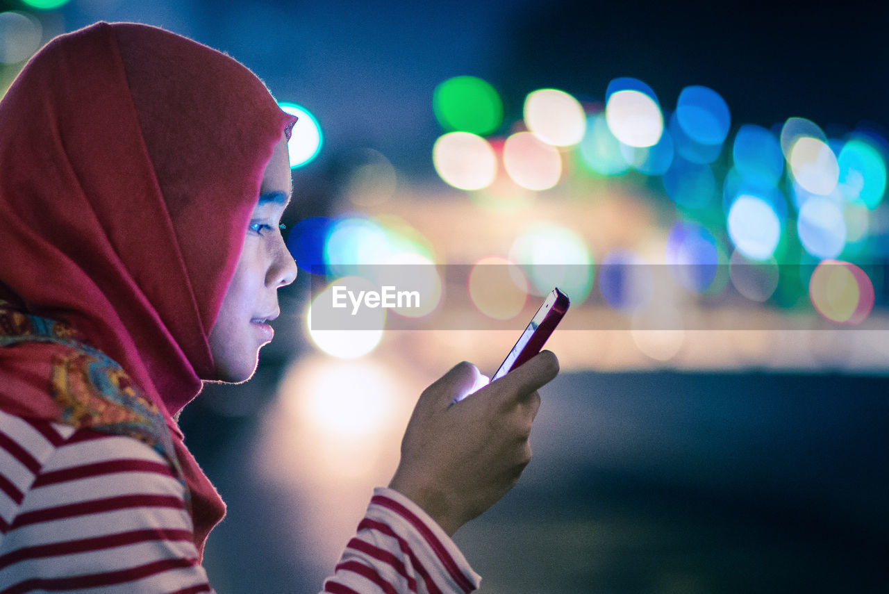 Profile of young woman using phone at night
