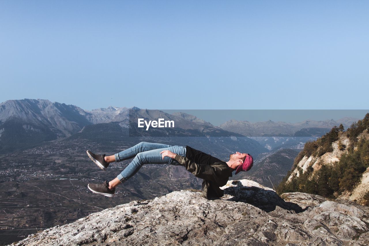 Man levitating over mountain against clear sky