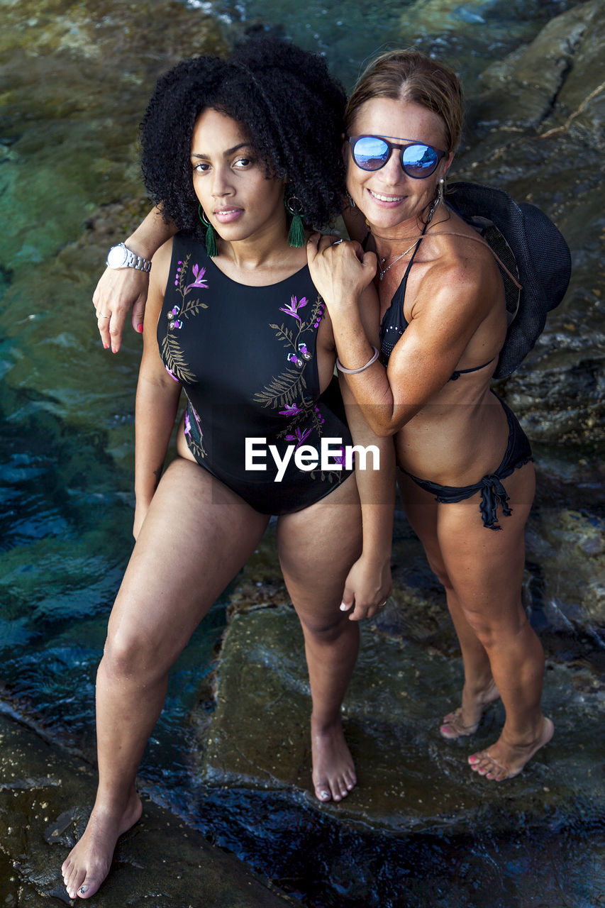 Portrait of mother and daughter in bikini standing on rock