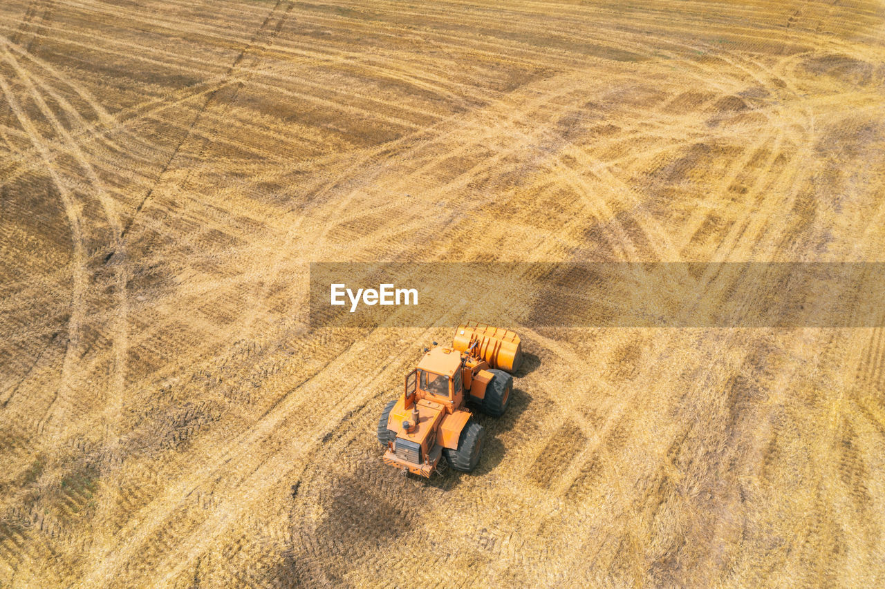 Orange tractor driving through the mown wheat field. farmers at work. agriculture harvesting season.