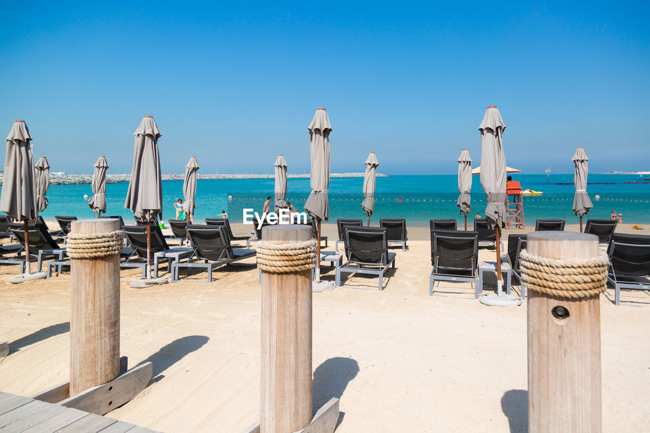 Wooden chairs on beach against clear blue sky