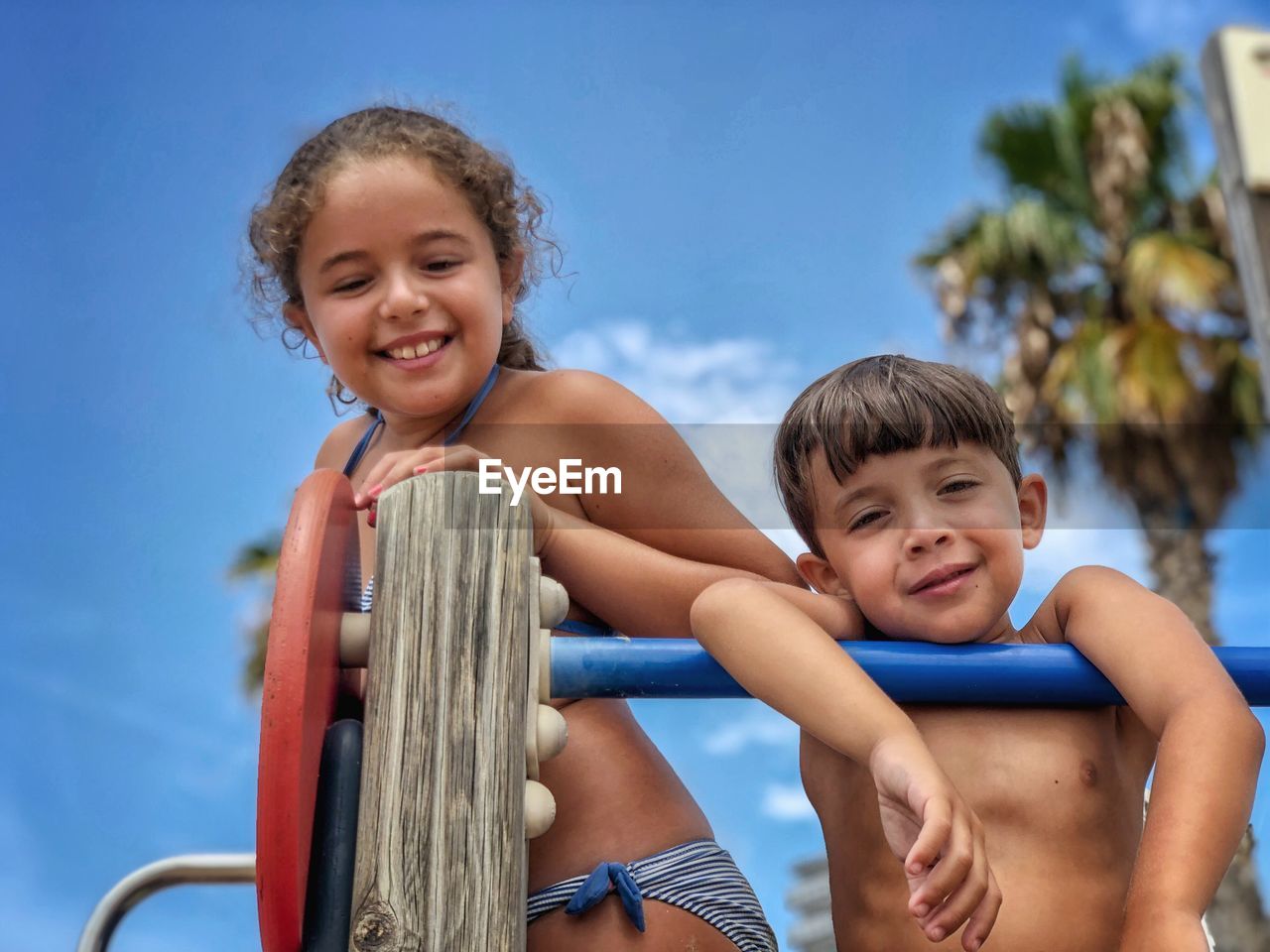 Portrait of happy siblings against blue sky