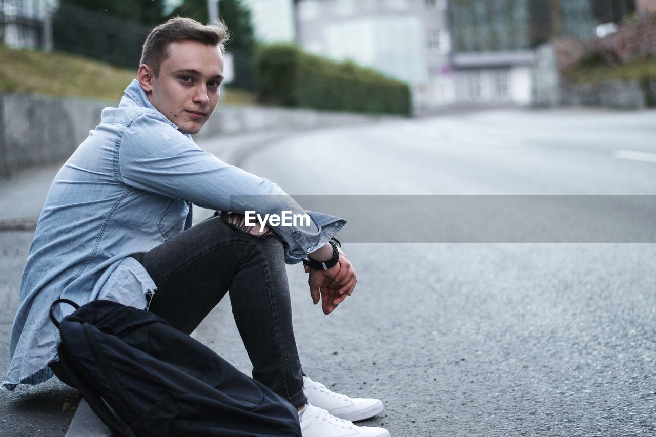 Side view portrait of young man sitting on road