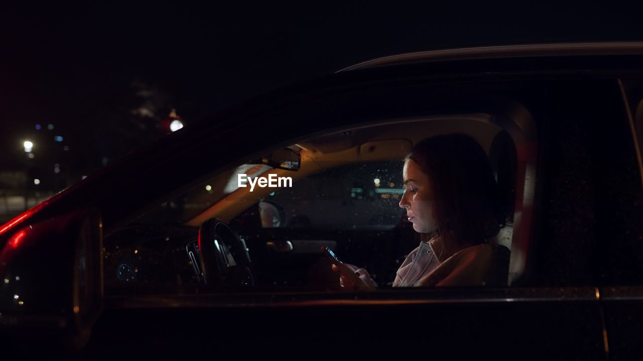 Beautiful business woman using smartphone in a car at night