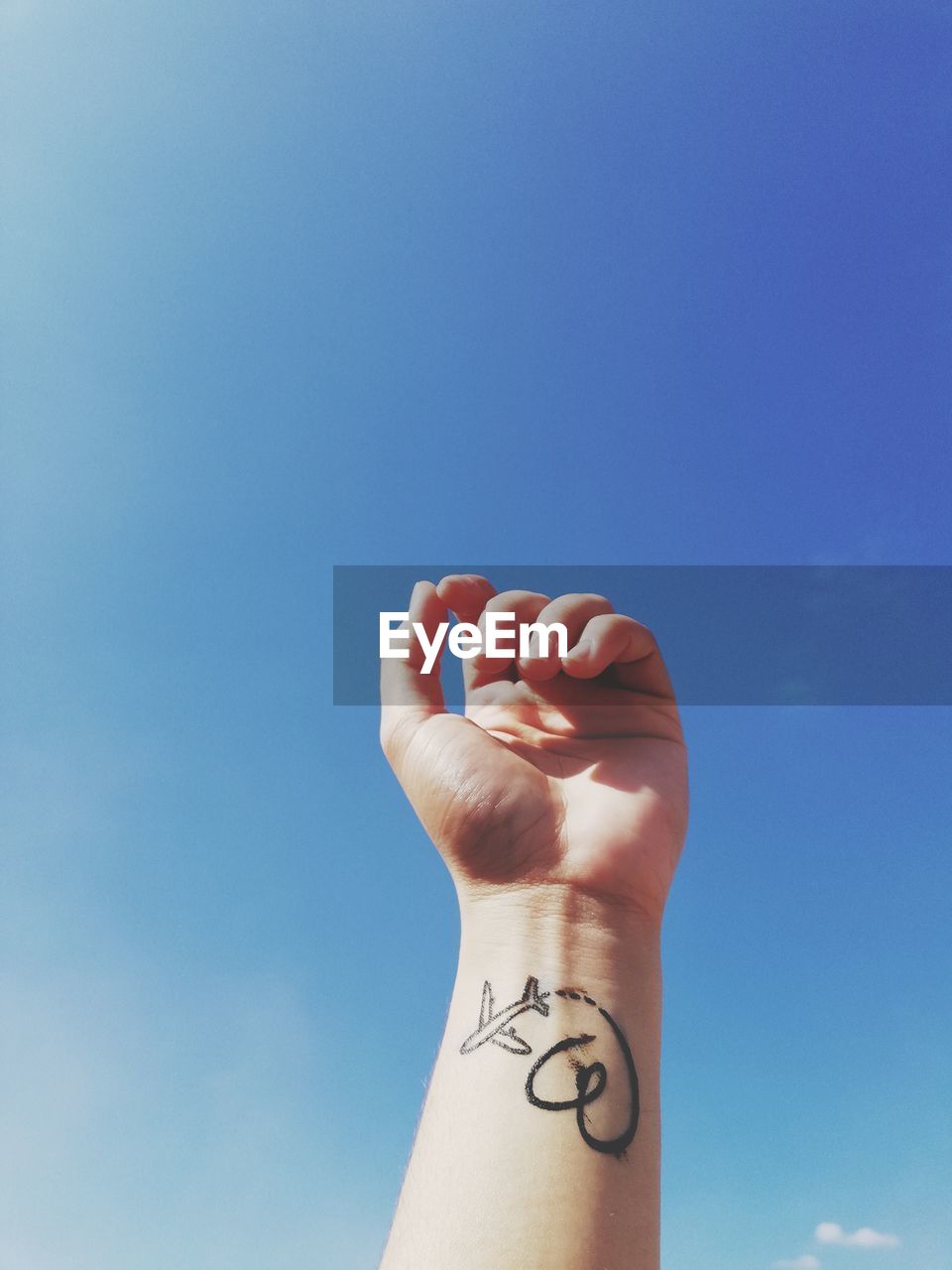 Cropped hand with tattoo against blue sky