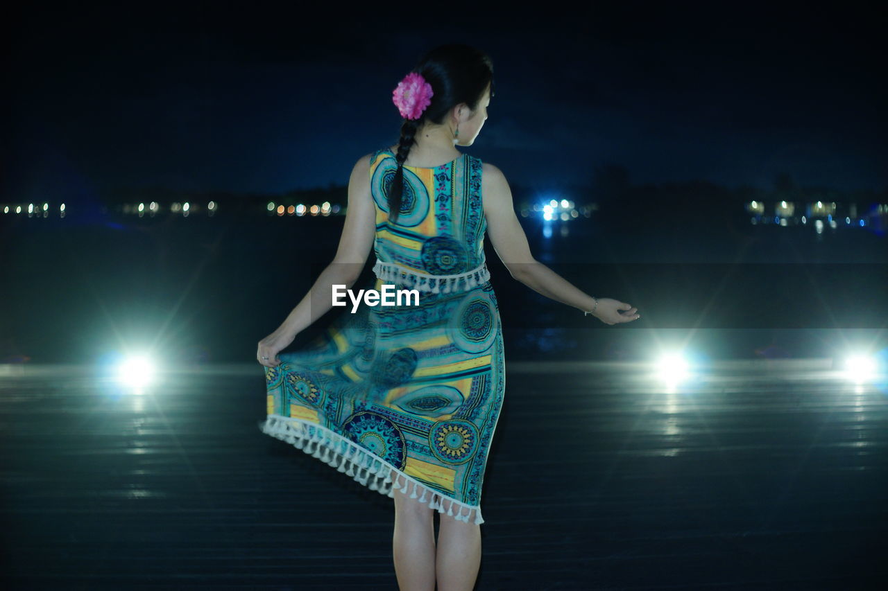 WOMAN ON ILLUMINATED LIGHTING EQUIPMENT AT NIGHT DURING FESTIVAL