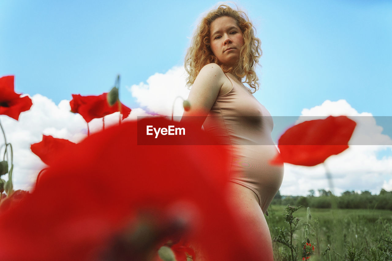 Side view of woman among red flowers on field against clear sky