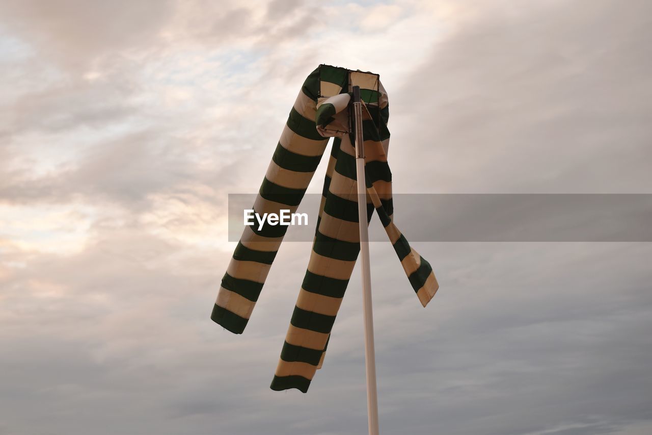Low angle view of windsock on pole against cloudy sky