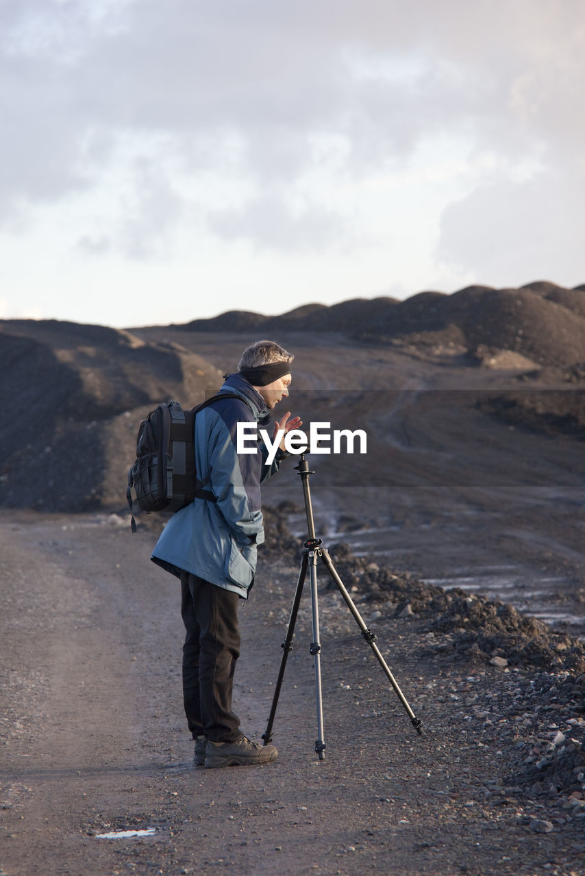 Side view of man photographing while standing against sky