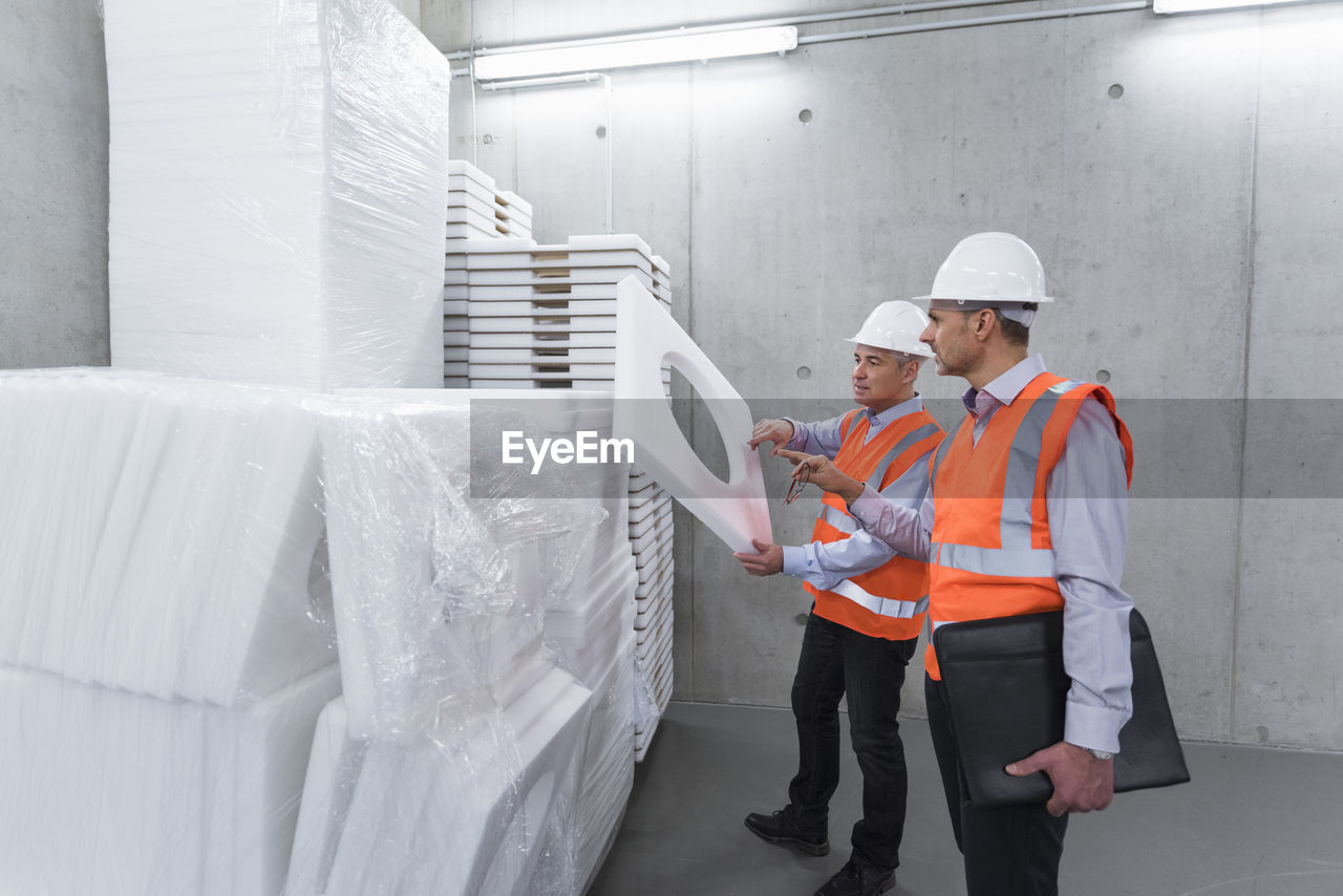 Two colleagues wearing safety vests and hard hats examining polystyrene