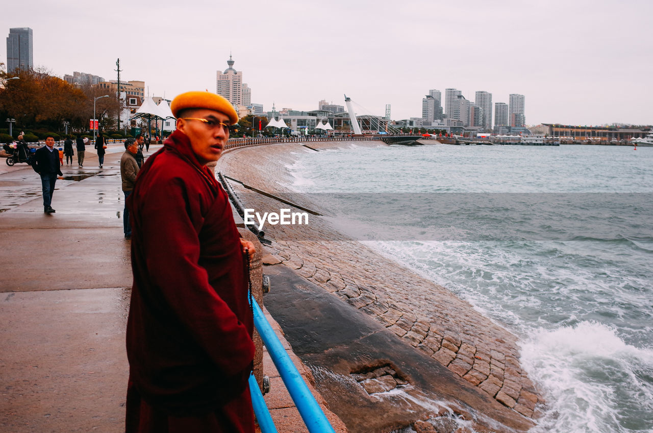 SIDE VIEW OF MAN STANDING BY SEA AGAINST SKY