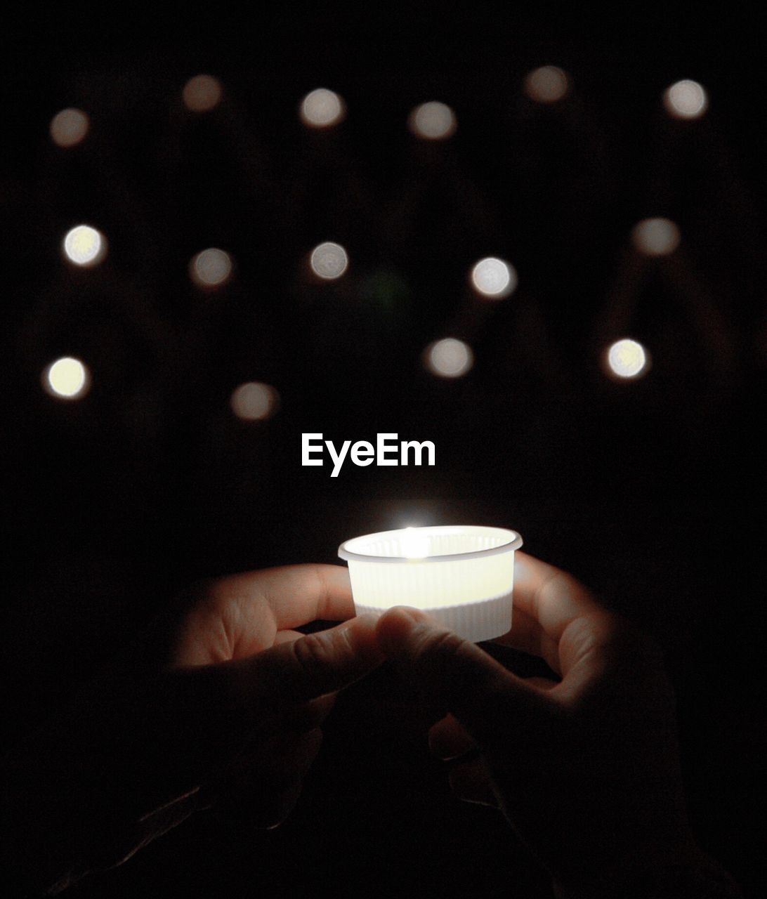 Close-up of hand holding candles in white plastic cup of lighting equipment