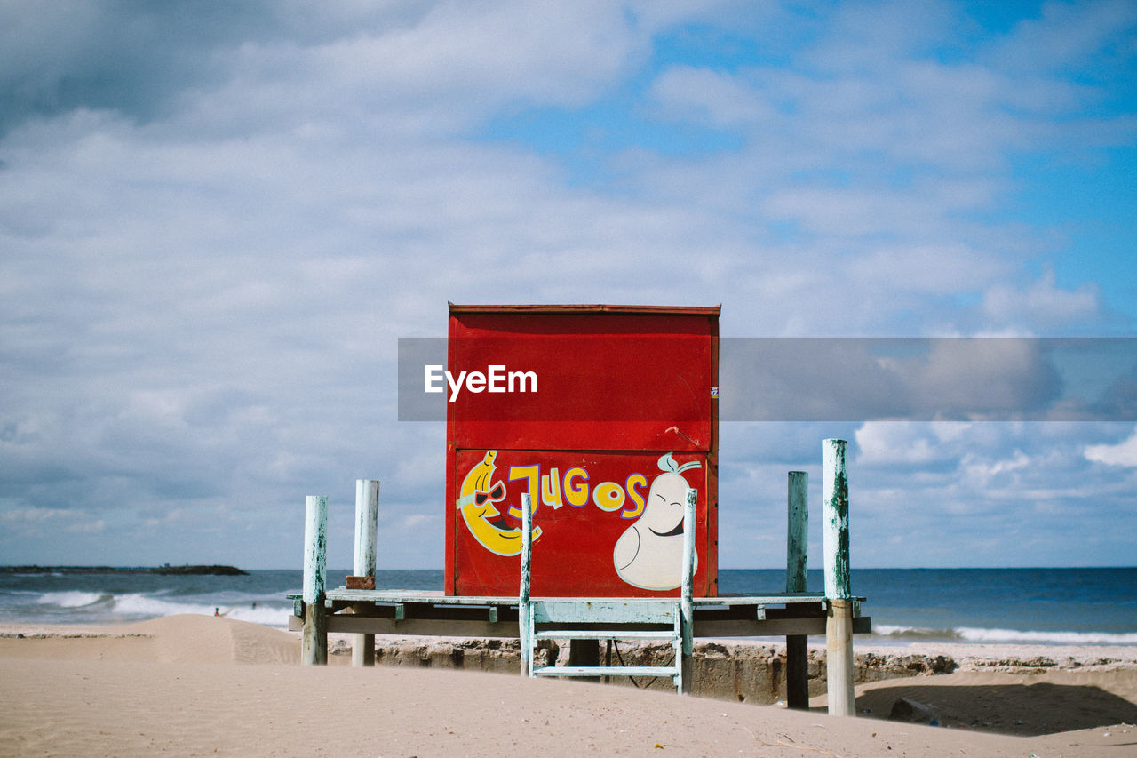 Red lifeguard hut on beach against cloudy sky