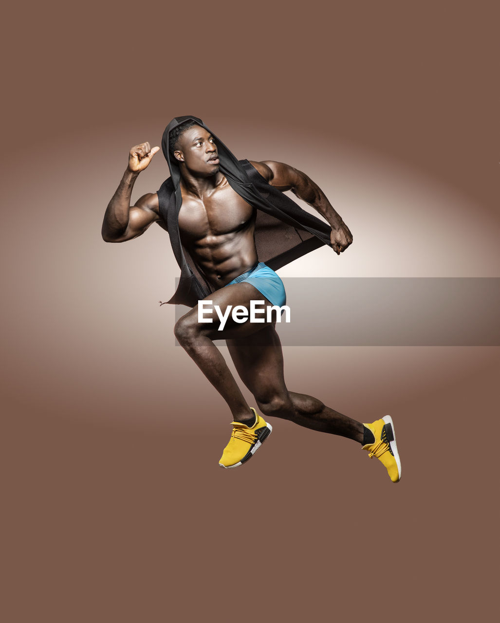 Full length of shirtless athlete jumping against brown background
