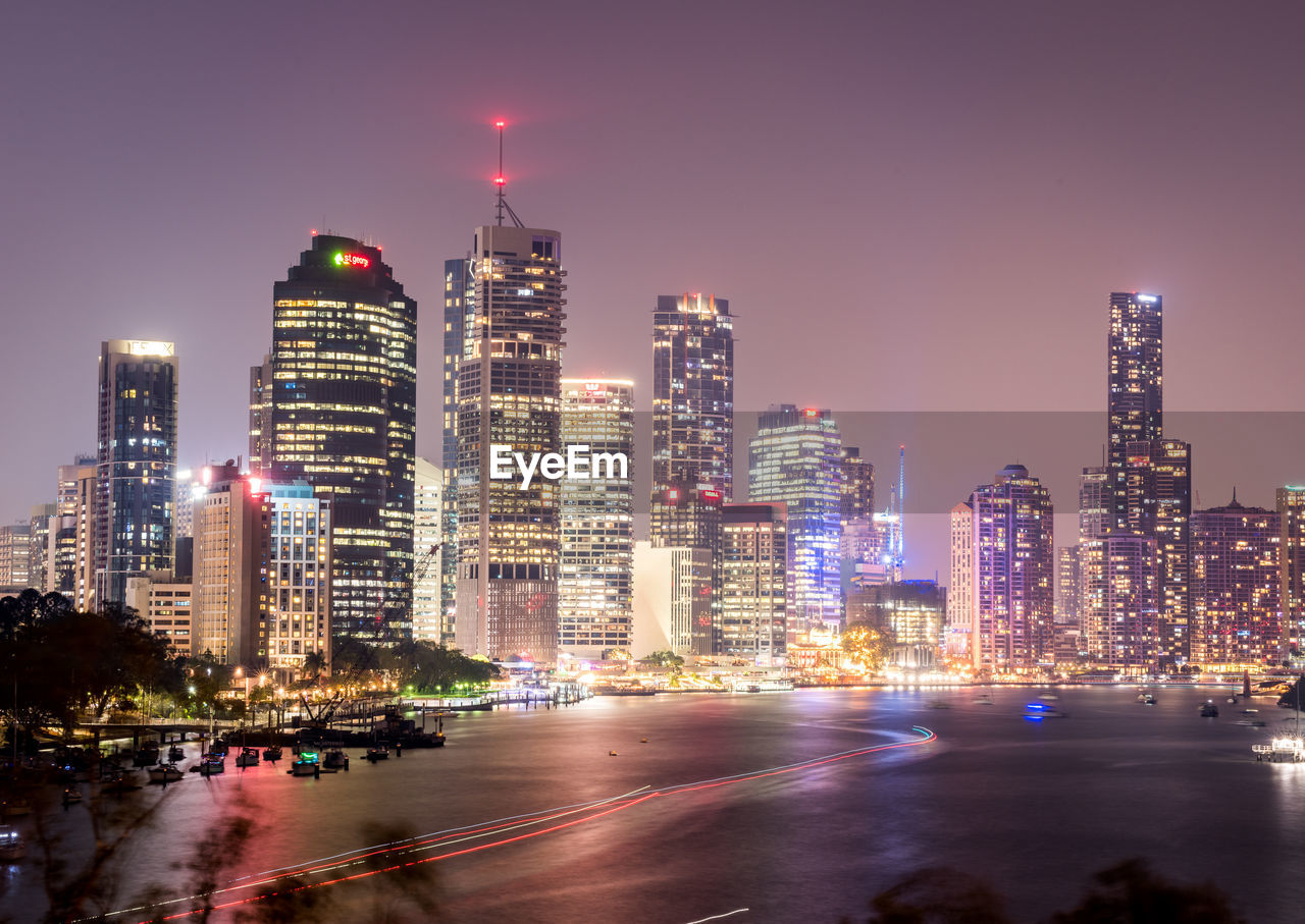 Illuminated modern buildings in city against sky at night