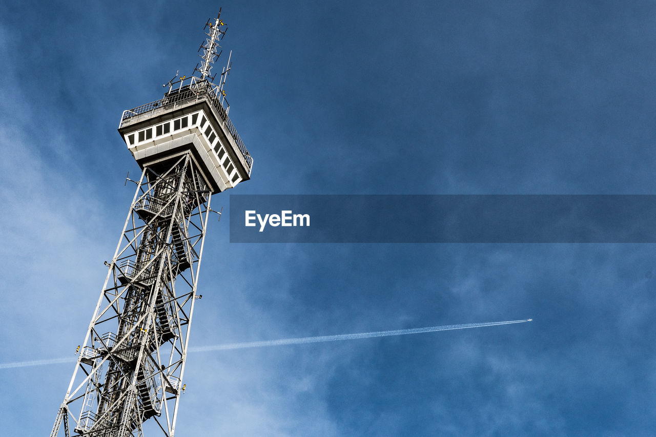 Low angle view of vapor trail against blue sky and a tower. 