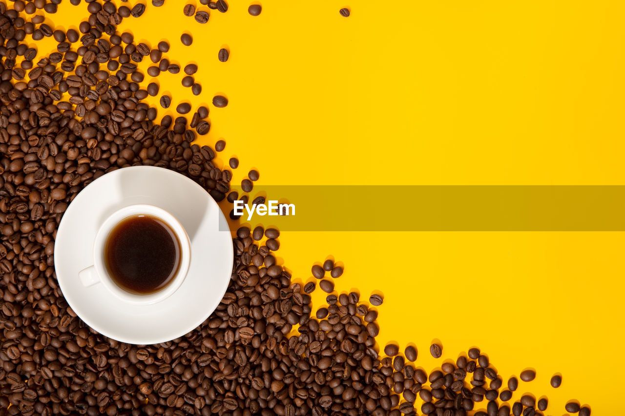 Coffee cup and roasted beans on yellow background. coffee background. top view copy space