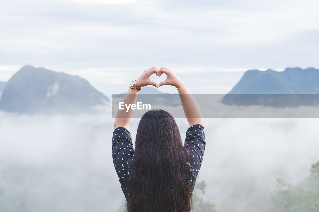 Rear view of woman making heart shape while looking at mountains
