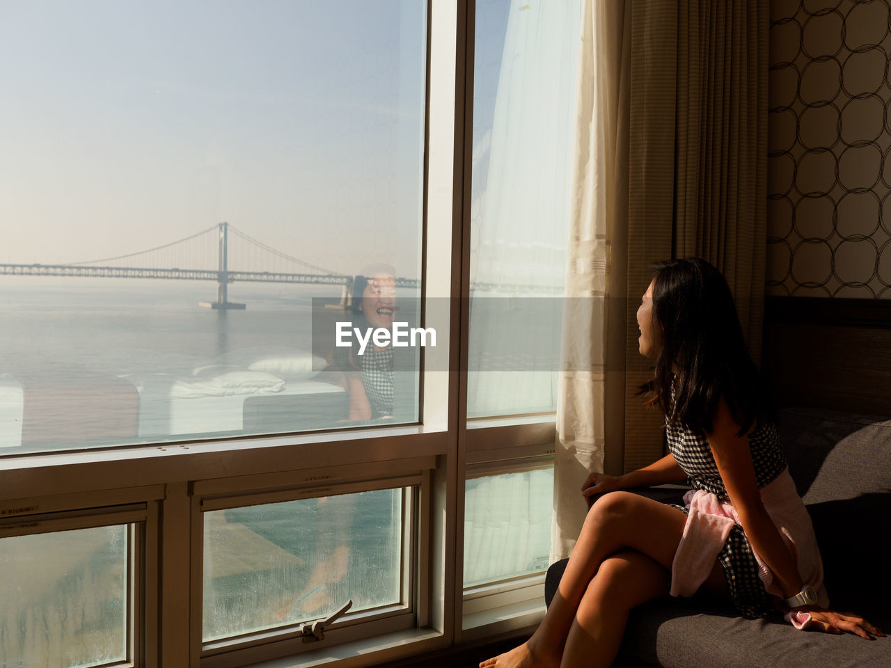 Woman looking through window while sitting on sofa at home