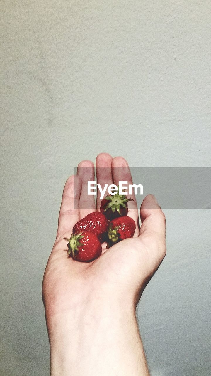 Cropped image of hand holding strawberries against wall