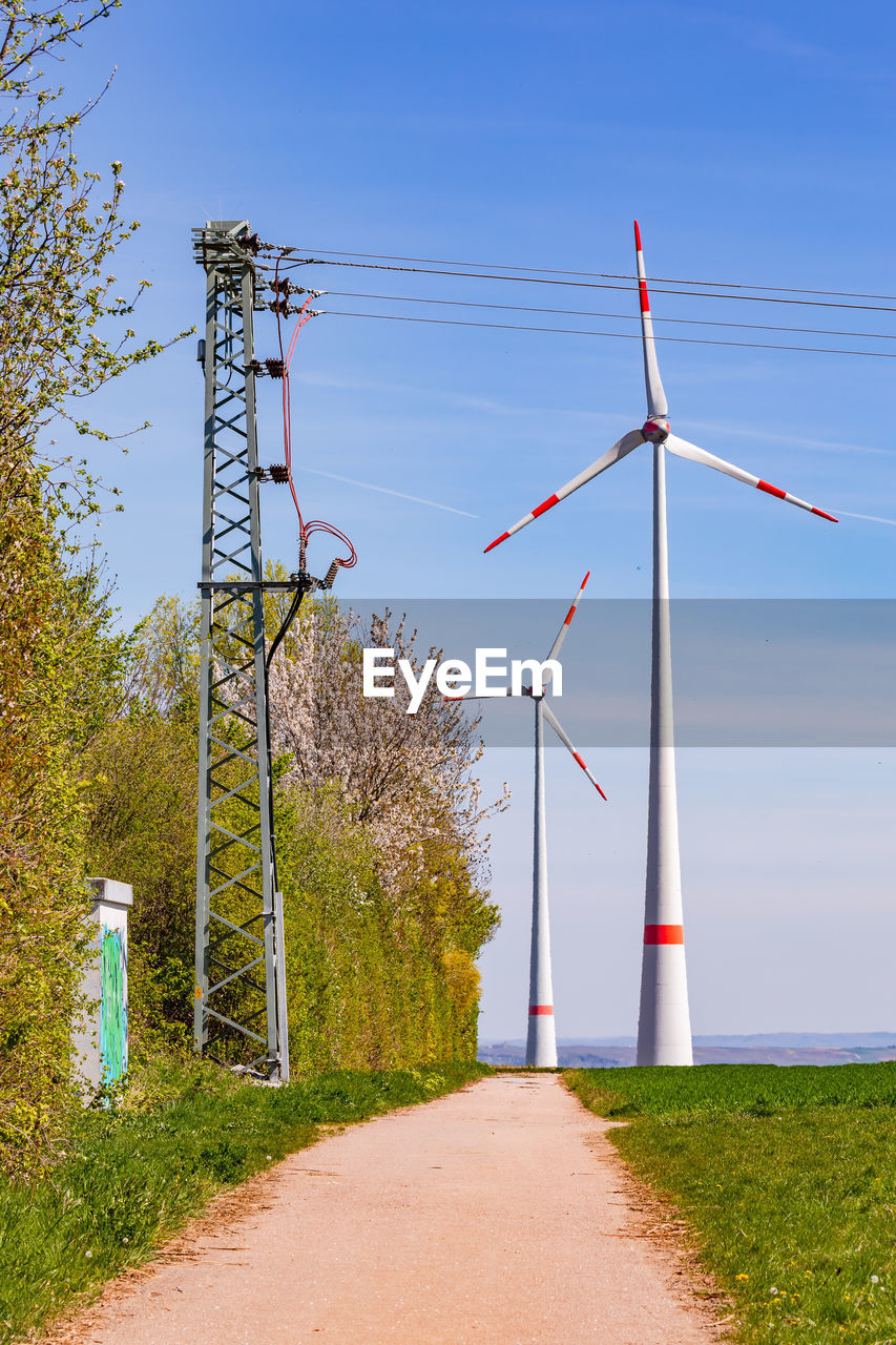 Wind turbines and electricity pylons for green electricity stand next to a dirt road, rural germany
