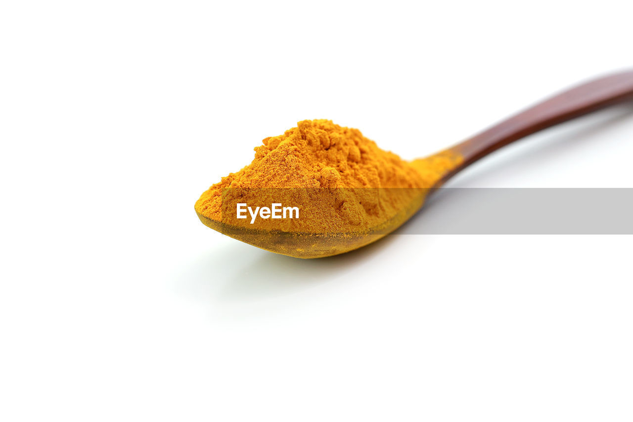 Close-up of turmeric spice in spoon against white background