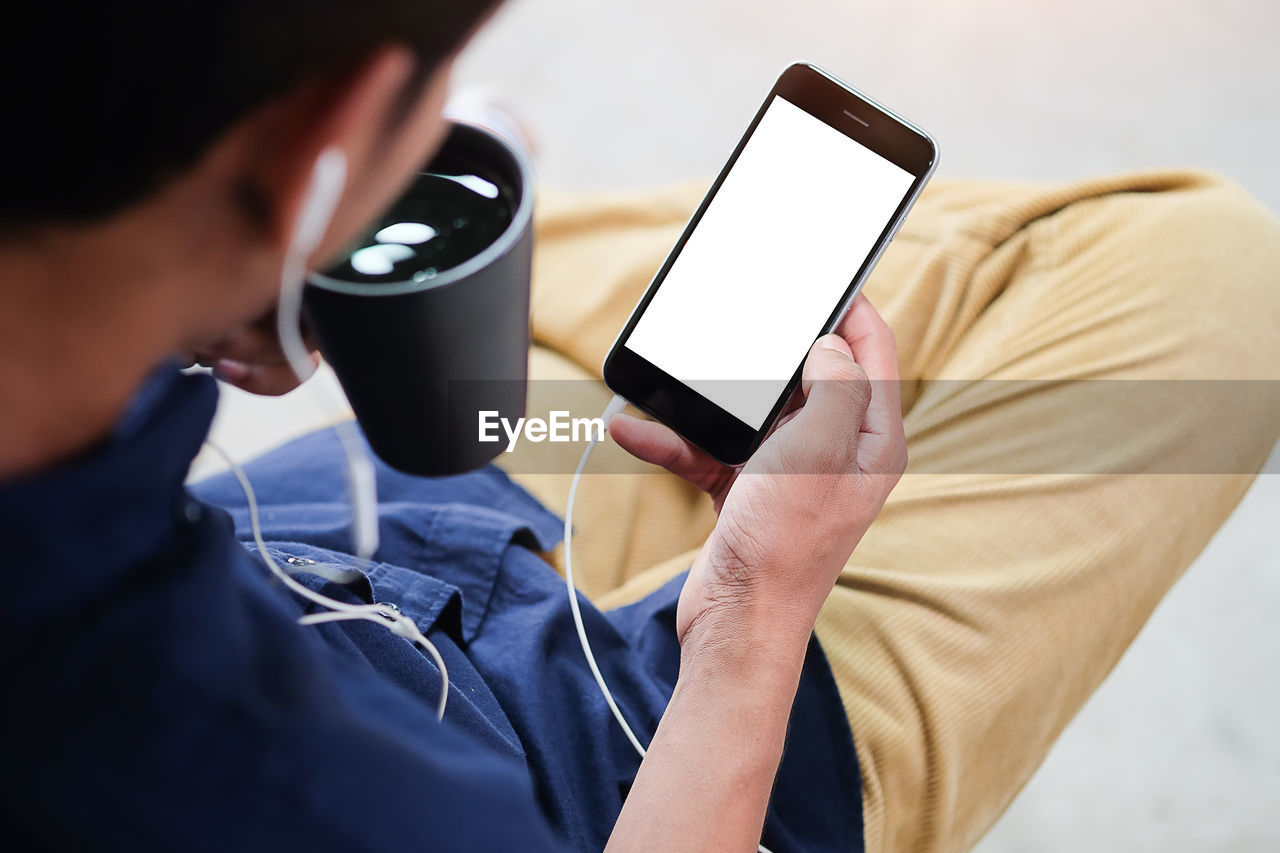 Low section of man with coffee cup using phone while sitting at home