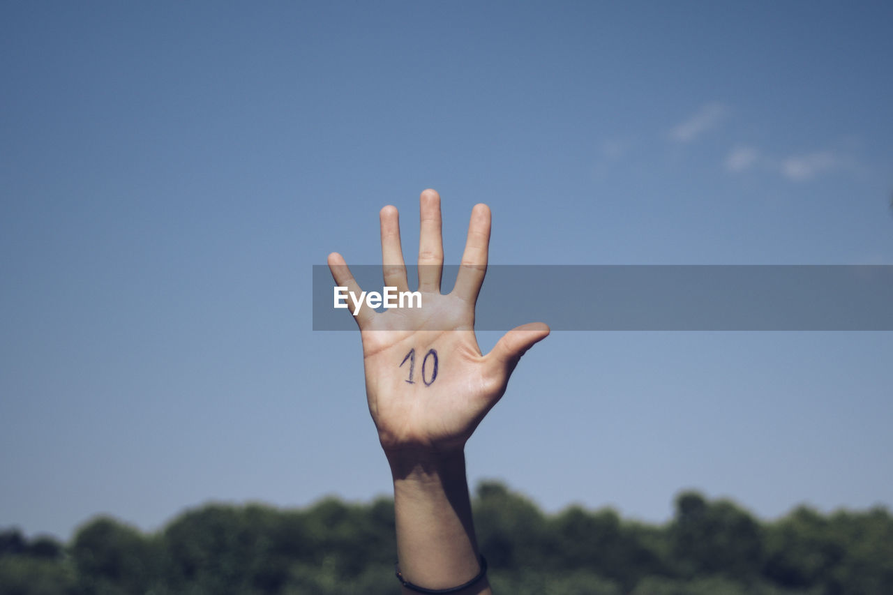 Cropped hand of person with numbers on palm against sky