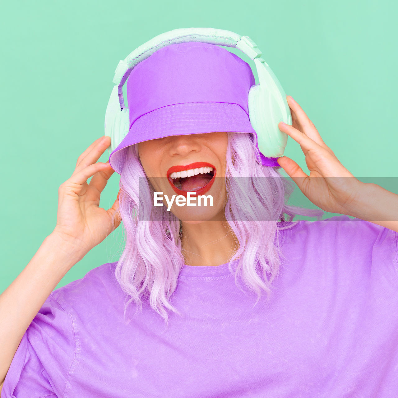 Side view of woman wearing hat and headphones against colored background