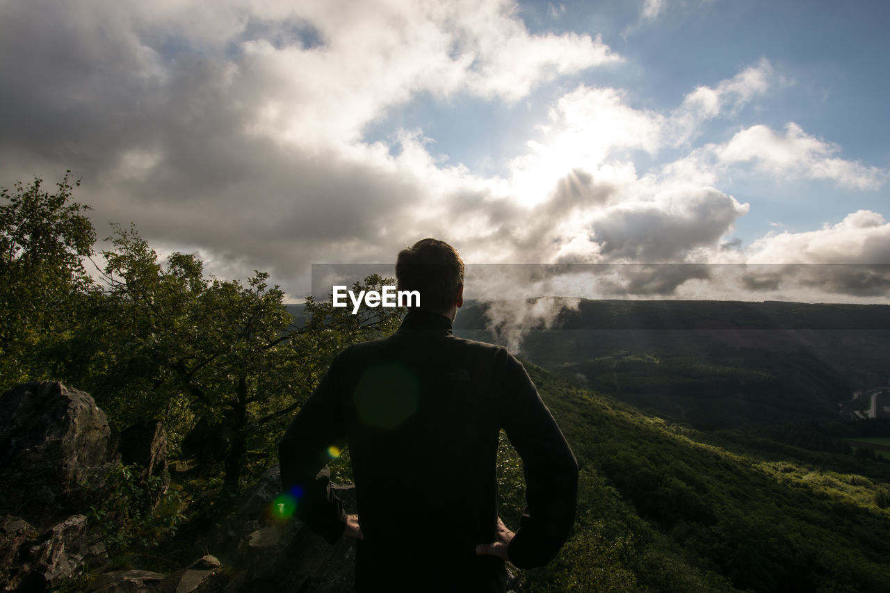 Rear view of man standing on cliff against landscape