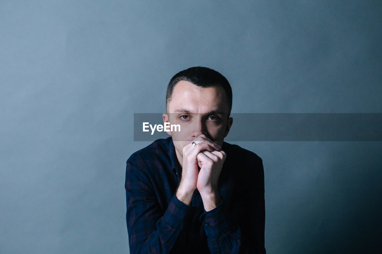 Portrait of man with hands covering mouth sitting against wall